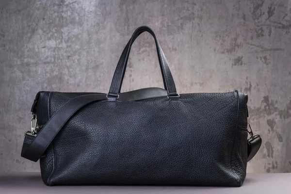 Чорна шкіряна сумка для подорожей, над фоном бетонної стіни — стокове фото
