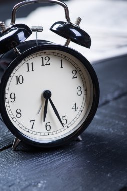 Ahşap bir masa üzerinde gazete ile siyah çalar saat