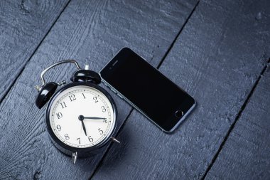 Ahşap bir masa cep telefonu ile siyah çalar saat
