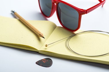 Kalem, güneş gözlüğü, dize ve arabulucu beyaz yüzeyi sarı not defteri