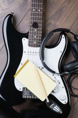 Elektro gitar, notedpad ve kalem kahverengi ahşap zemin üzerinde kulaklık ile