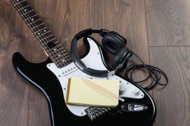 Elektro gitar, notedpad ve kalem kahverengi ahşap zemin üzerinde kulaklık ile