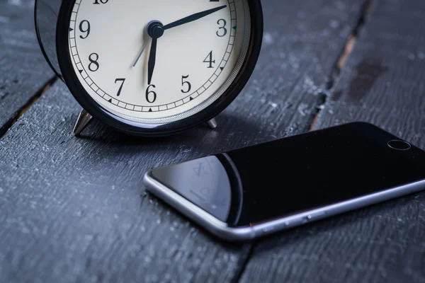 Ahşap bir masa cep telefonu ile siyah çalar saat