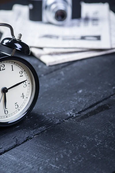 Black alarm clock with camera and newspaper on a wooden table — Stock Photo, Image