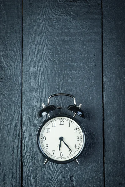 Alarm clock on a black wooden surface — Stock Photo, Image