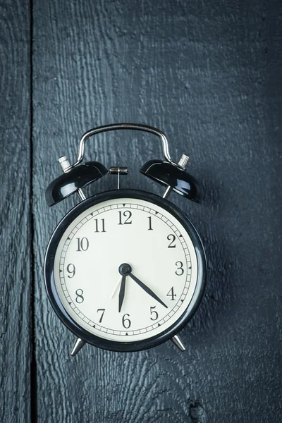 Alarm clock on a black wooden surface — Stock Photo, Image