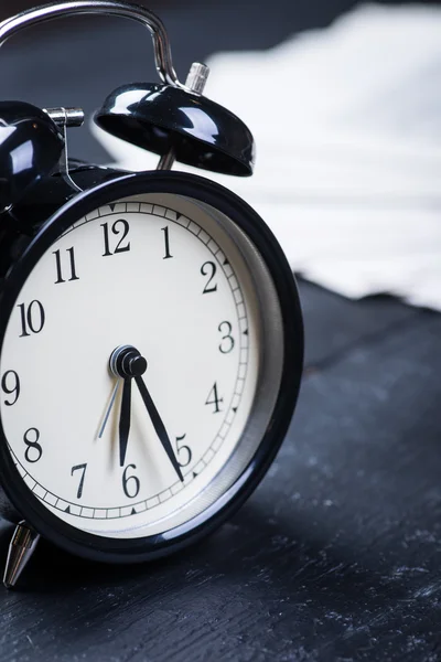 Black alarm clock with newspaper on a wooden table — Stock Photo, Image