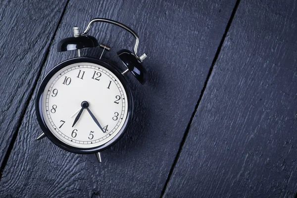 Relógio despertador em uma superfície de madeira preta — Fotografia de Stock