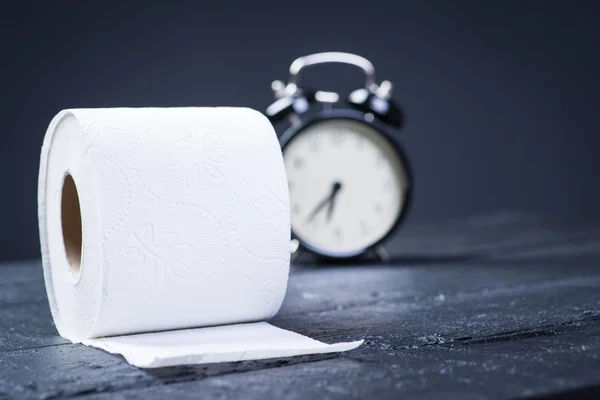 Alarm clock with toilet paper on a black wooden table — Stock Photo, Image