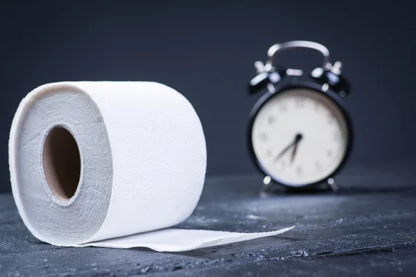 Alarm clock with toilet paper on a black wooden table — Stock Photo, Image