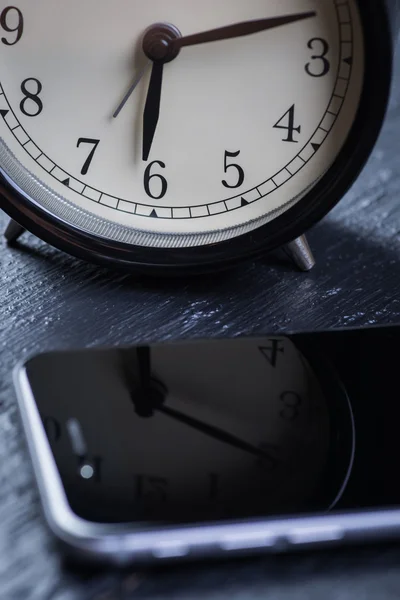 Reloj despertador negro con teléfono celular en una mesa de madera — Foto de Stock