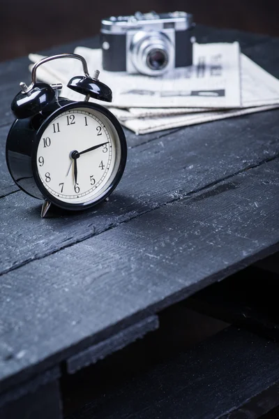 Reloj despertador negro con cámara y periódico sobre una mesa de madera — Foto de Stock