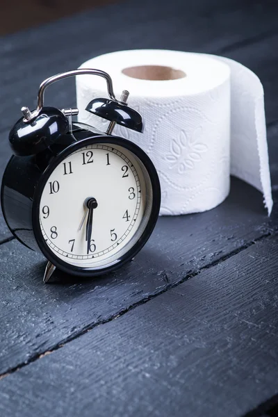 Wecker mit Toilettenpapier auf schwarzem Holztisch — Stockfoto