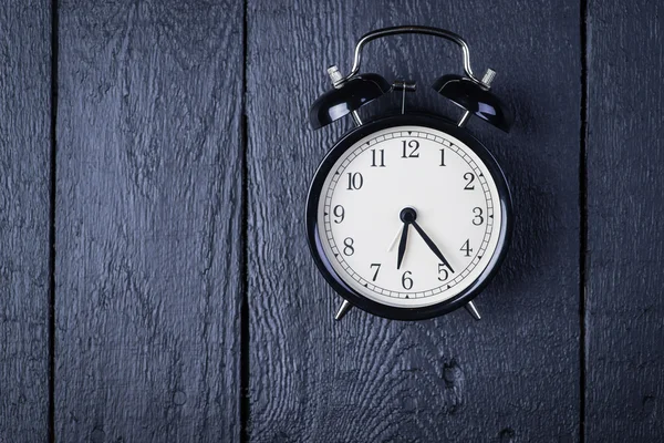 Alarm clock on a black wooden surface — Stock Photo, Image