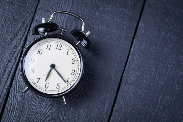 Alarm clock on a black wooden surface — Stock Photo, Image