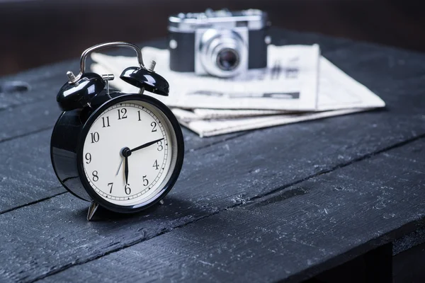 Reloj despertador con cámara y periódico en la mesa — Foto de Stock