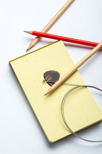 Yellow notepad with three pencils, string and mediator on white surface — Stock Photo, Image
