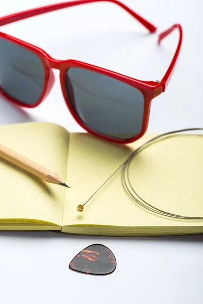 Yellow notepad with pencil, sunglasses, string and mediator on white surface — Stock Photo, Image