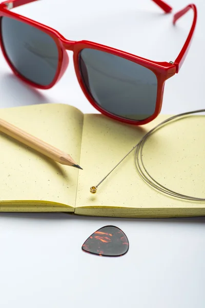 Yellow notepad with pencil, sunglasses, string and mediator on white surface — Stock Photo, Image