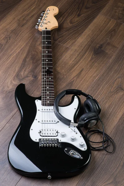 Electric guitar with headphones on a brown wooden floor — Stock Photo, Image