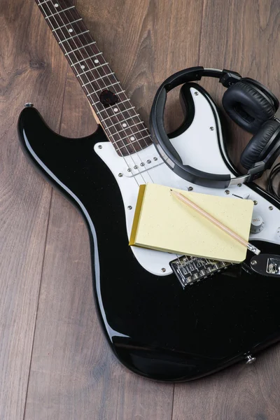Electric guitar with headphones, notedpad and pencil on a brown wooden floor — Stock Photo, Image