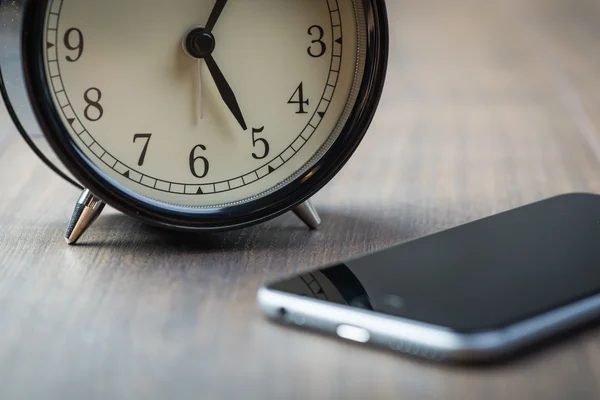 Reloj despertador vintage negro con teléfono en un piso de madera — Foto de Stock