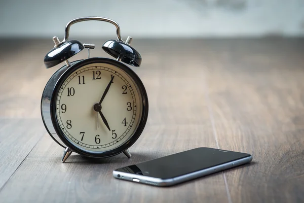 Relógio de alarme vintage preto com telefone em um piso de madeira — Fotografia de Stock