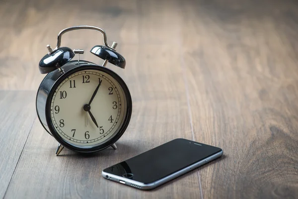 Black vintage alarm clock with phone on a wooden floor