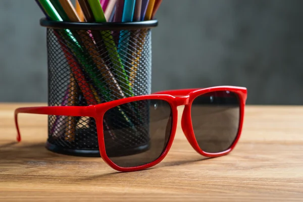 Red sun glasses with bunch of color pencils in a stand — Stock Photo, Image