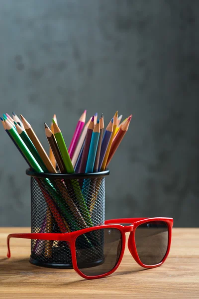 Rudé slunce brýle s bandou barevných tužek na stojanu — Stock fotografie