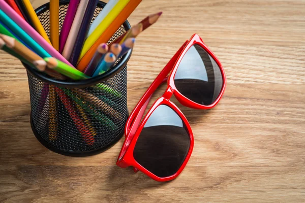 Red sun glasses with bunch of color pencils in a stand — Stock Photo, Image