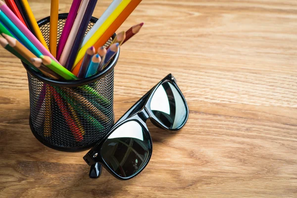 Gafas de sol negras con manojo de lápices de color en un soporte — Foto de Stock