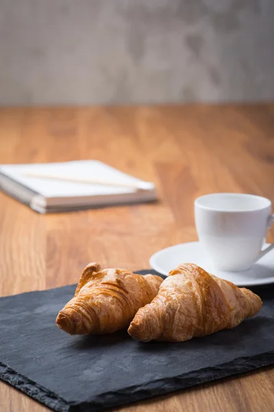Dvě chutné francouzské croissanty s šálkem kávy a notebook — Stock fotografie
