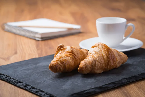 Dos sabrosos croissants franceses con una taza de café y un cuaderno —  Fotos de Stock