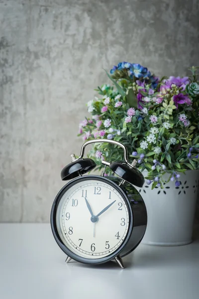 Starý budík na bílý stůl s květinami — Stock fotografie
