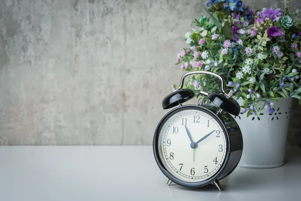 Althergebrachter Wecker auf weißem Tisch mit Blumen — Stockfoto