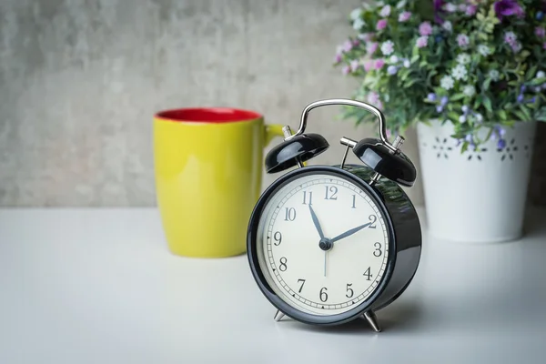 Althergebrachter Wecker auf weißem Tisch mit Blumen und Kaffeetasse — Stockfoto