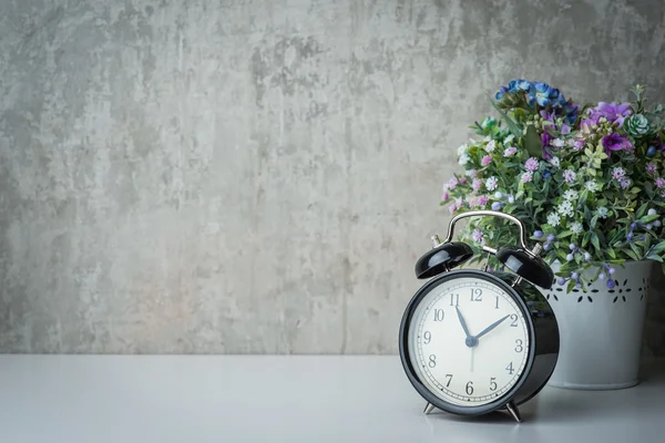 Old-time alarm clock on a white table with flowers — Stock Photo, Image