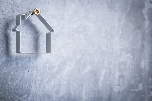 Casa metálica colgando del tornillo en la pared de hormigón gris —  Fotos de Stock