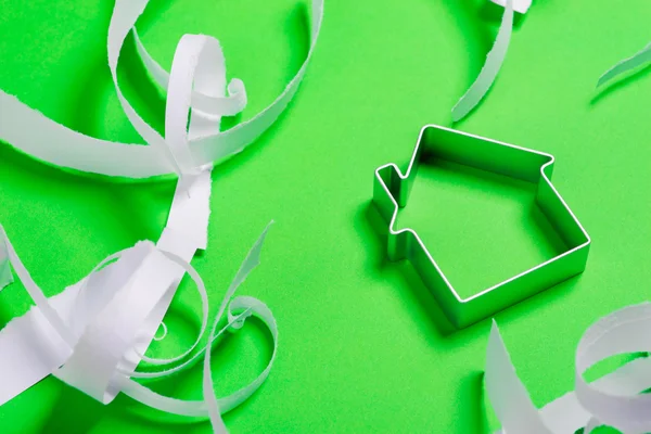 Metal house standing on a green surface with teared paper pieces — Stock Photo, Image