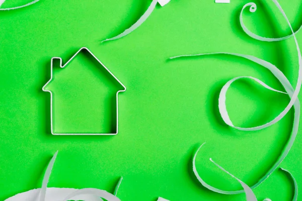 Metal house standing on a green surface with teared paper pieces — Stock Photo, Image