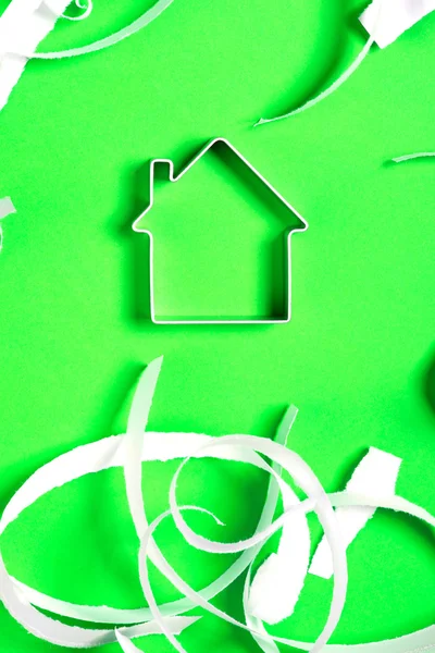 Metal house standing on a green surface with teared paper pieces — Stock Photo, Image