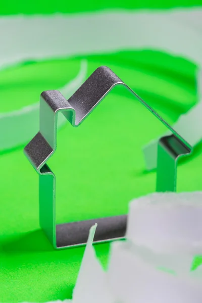 Metal house standing on a green surface with teared paper pieces — Stock Photo, Image