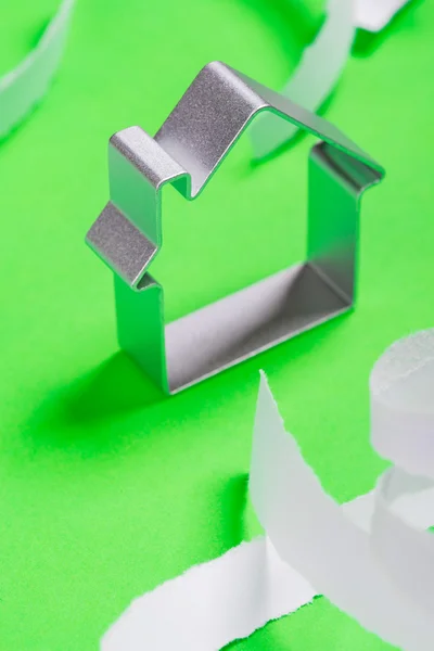 Kovové dům, stojící na zeleném povrchu s teared papírky Stock Obrázky
