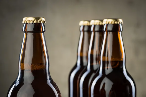 Bouteilles de bière fraîchement brassées en rangée sur le mur de béton gris — Photo