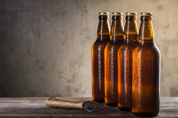 Freshly brewed beer bottles in a row with opener over the grey concrete wall — Stock Photo, Image
