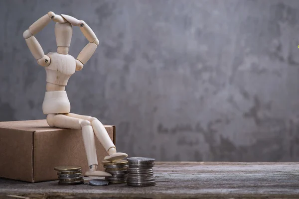 Small wooden dummy with sitting with coins over the grey concrete wall — Stock Photo, Image