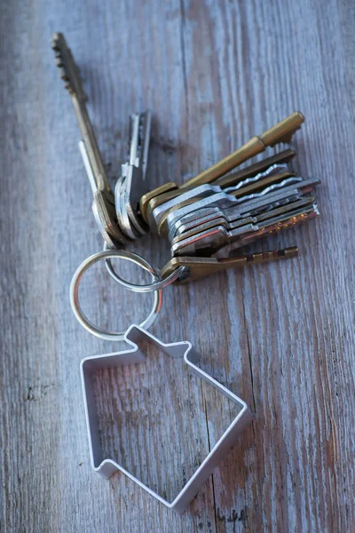 Um monte de chaves velhas desgastadas com casa de metal na superfície de madeira — Fotografia de Stock