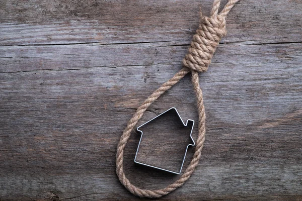 Small house framed with hangman's noose on brown wooden surface — Stock Photo, Image