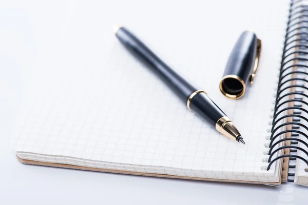 Um caderno espiral com caneta esferográfica preta sobre o fundo branco, isolado — Fotografia de Stock